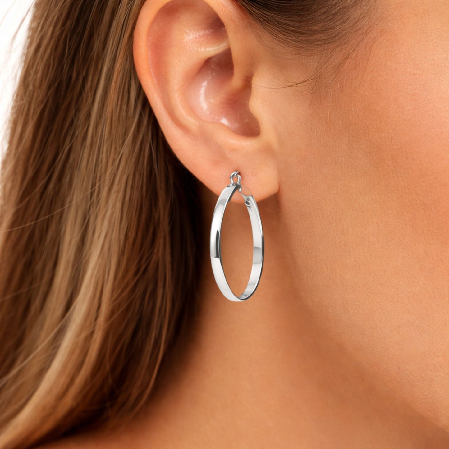 Silver hoop earring worn by a person with brown hair.