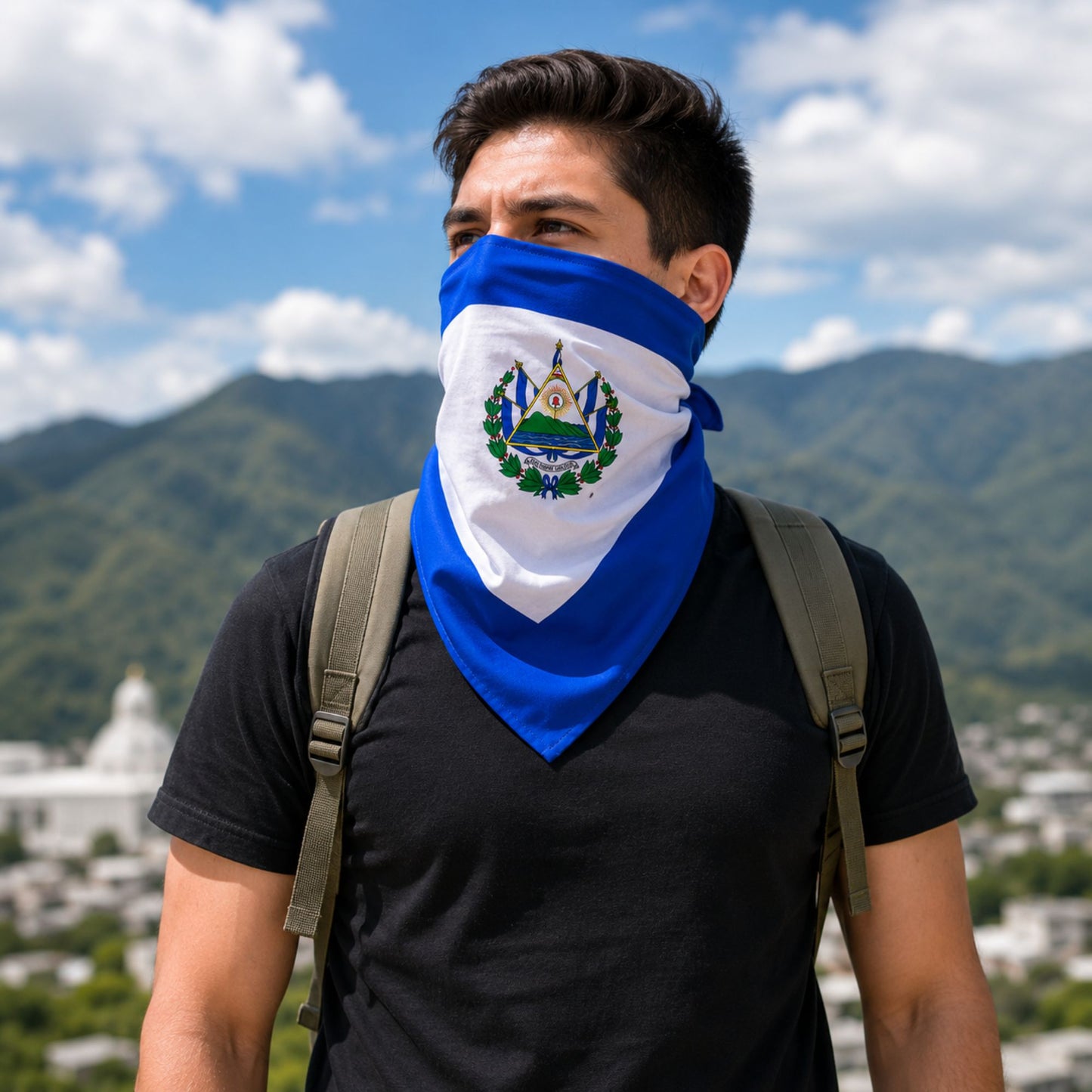 A man wearing a blue and white bandana face covering with the emblem of El Salvador, set against a background of mountains and a blue sky.