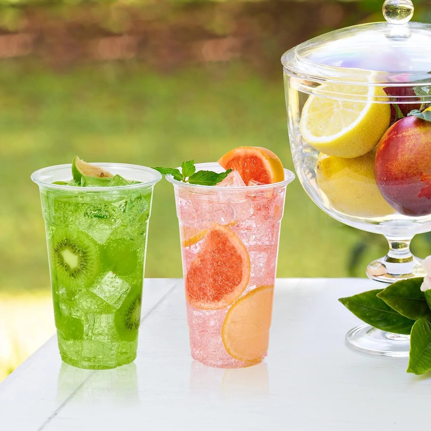 Two glasses of fruit-infused drinks on a table with a blurred natural background