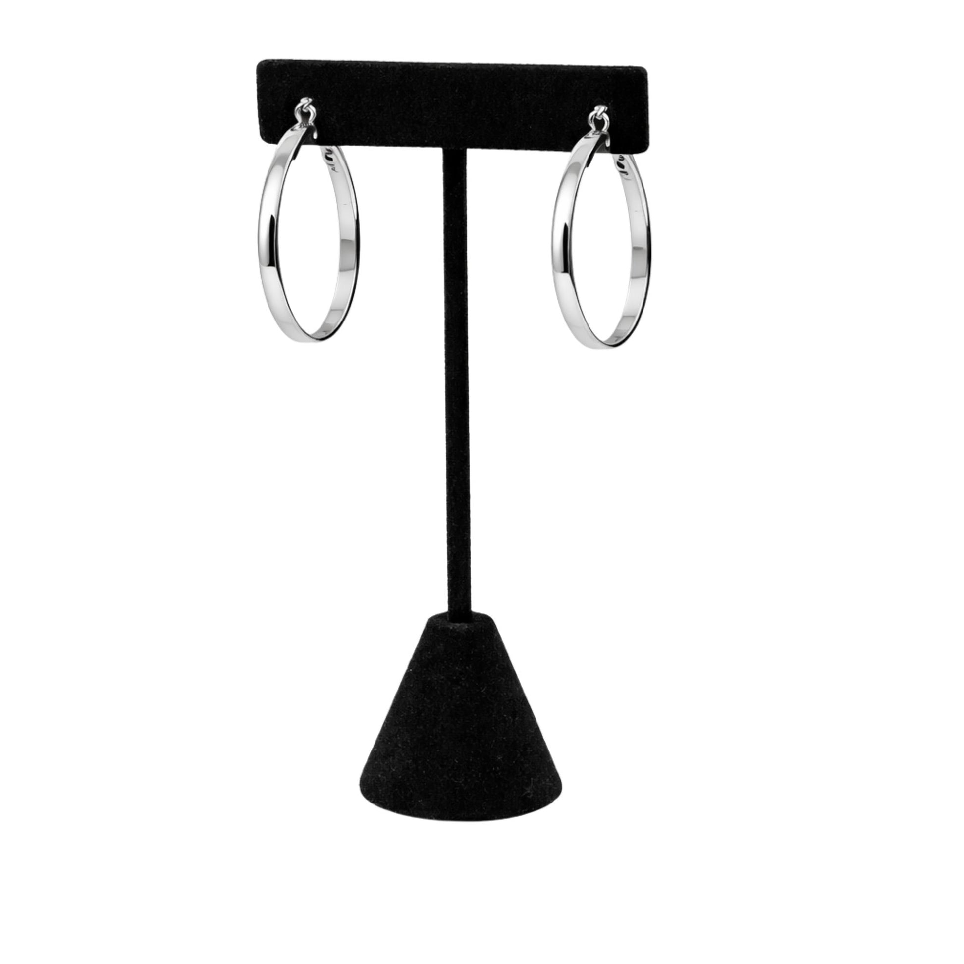Silver hoop earrings on a black earring stand against a white background