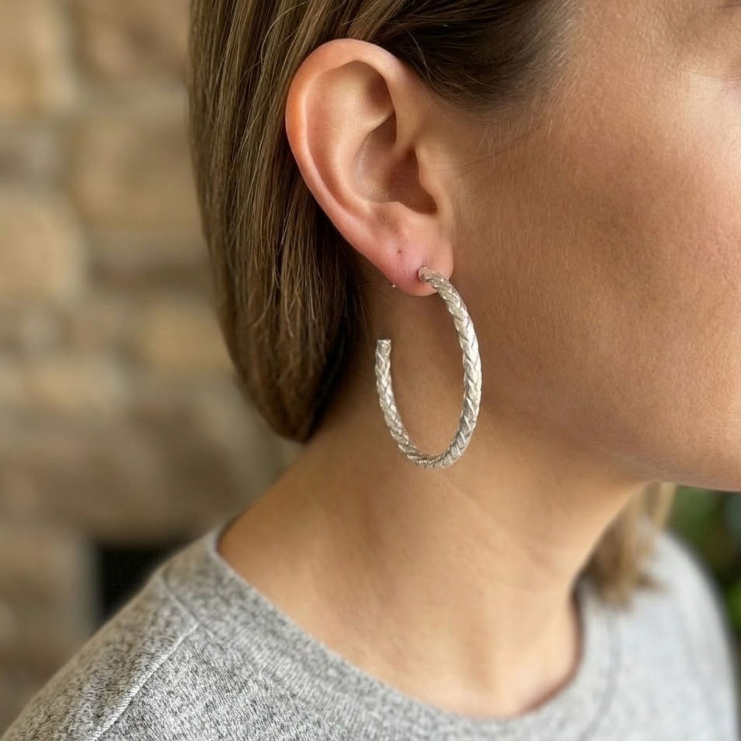 Close-up of a person wearing a silver hoop earring with a blurred stone wall background
