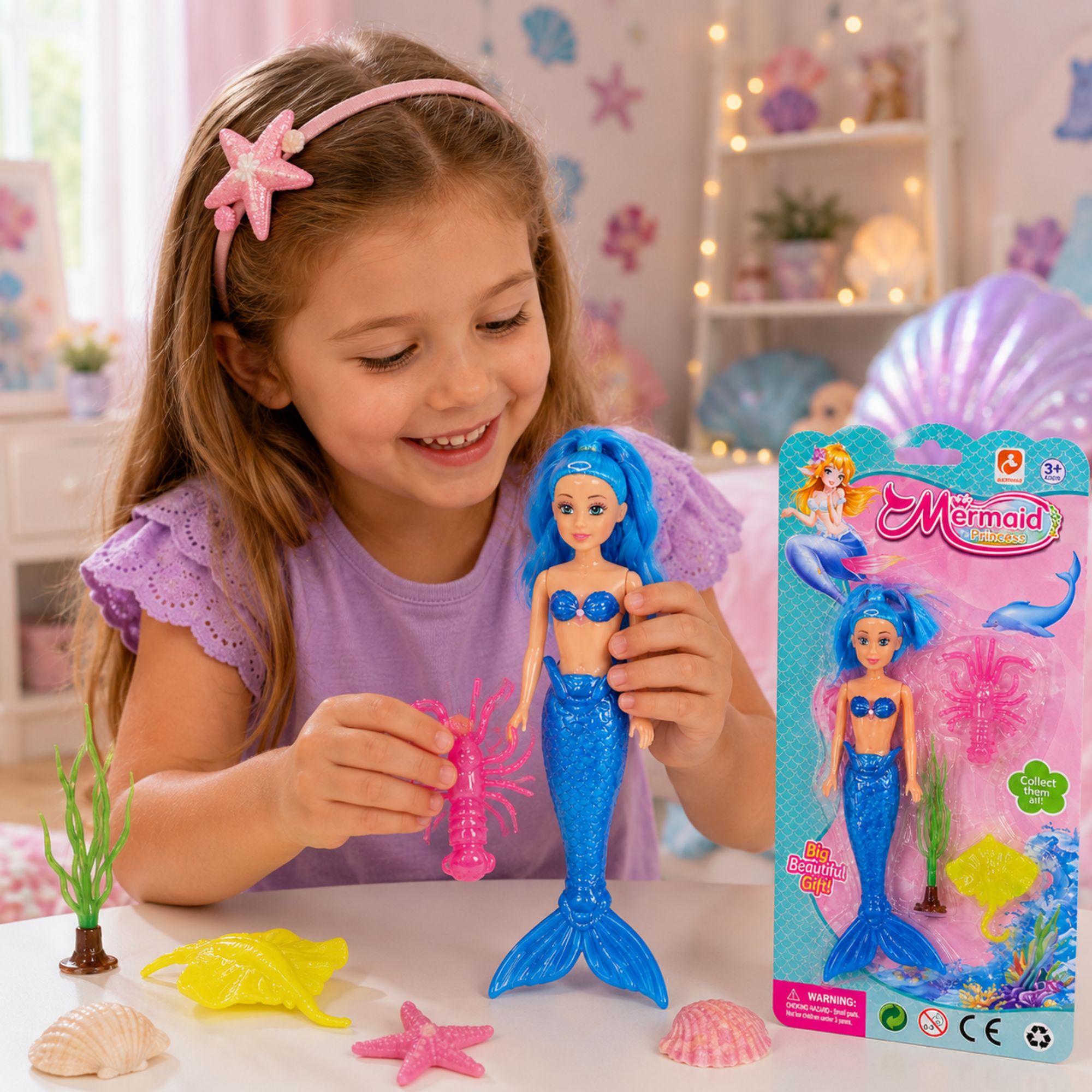 A young girl with a pink starfish headband smiles while holding a blue mermaid toy and its retail packaging on a white table. The scene is decorated with pink and blue mermaid-themed items, including seashells, a yellow starfish, and underwater garden accessories.