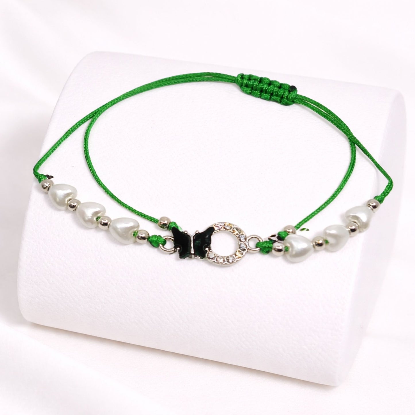 Green bracelet with beads and a butterfly charm on a white background
