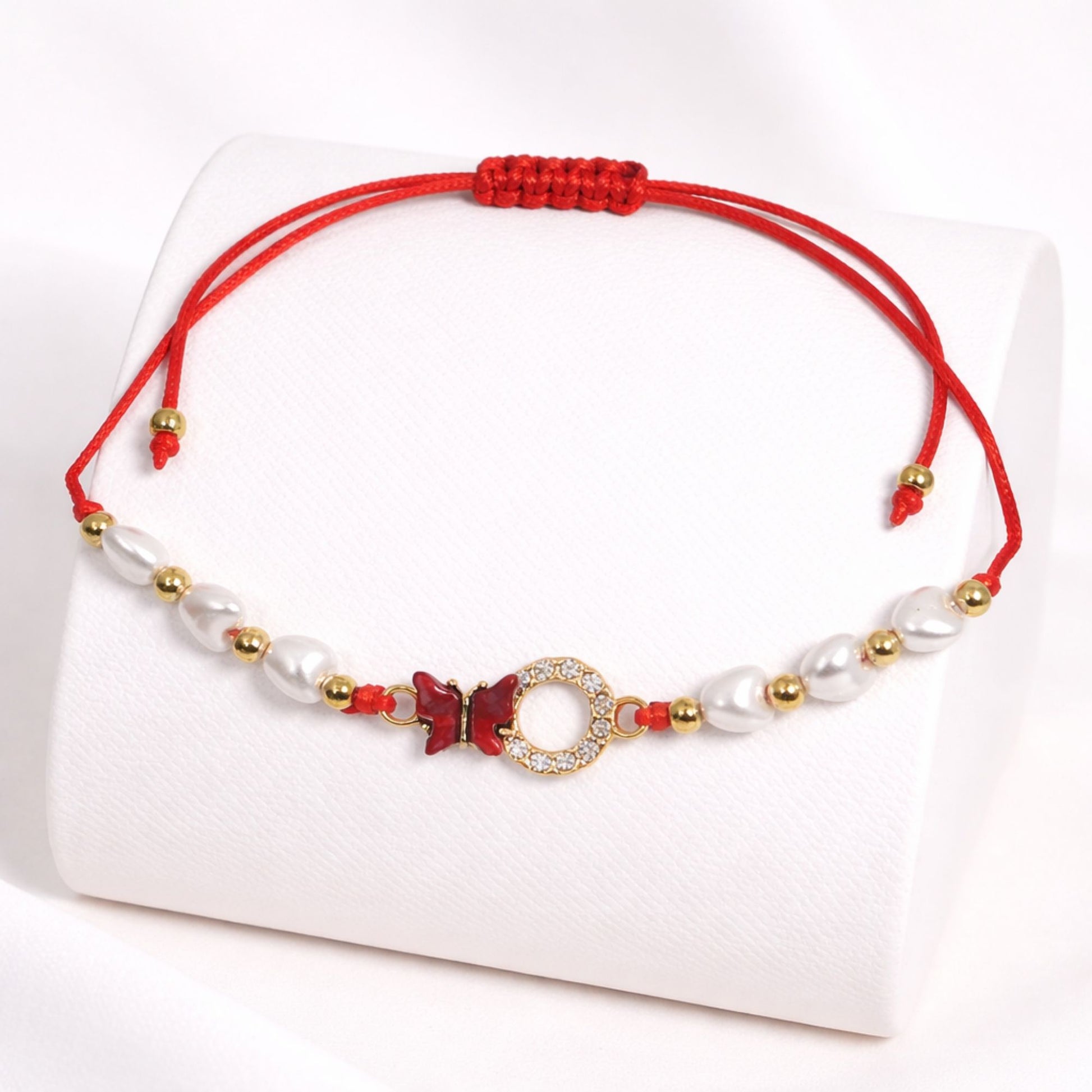 Bracelet with red cord, pearls, and gold accents on a white background