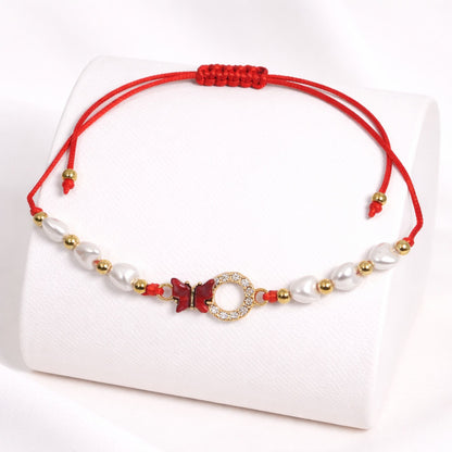 Bracelet with red cord, pearls, and gold accents on a white background