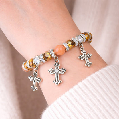 Bracelet with cross charms on a wrist against a neutral background
