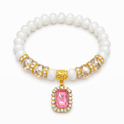 Pearl bracelet with gold and pink gemstone charm on a white background