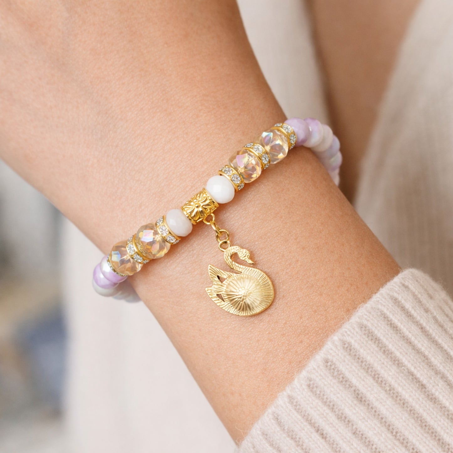 Bracelet with gold swan charm and multicolored beads on a wrist.