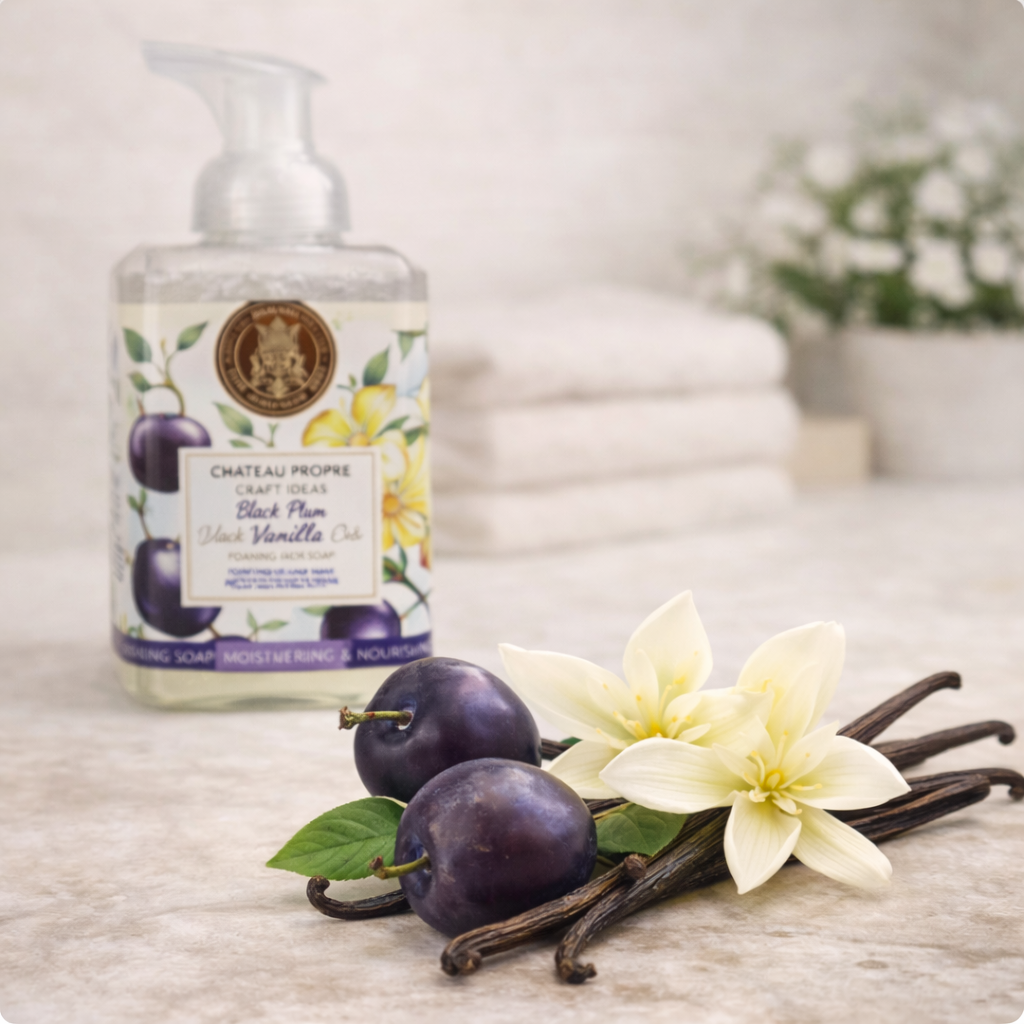 Foaming hand soap bottle with plums, vanilla beans, and flowers on a wooden surface.