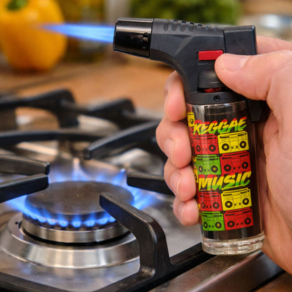 Hand holding a butane lighter with 'Reggae Music' design in front of a gas stove.