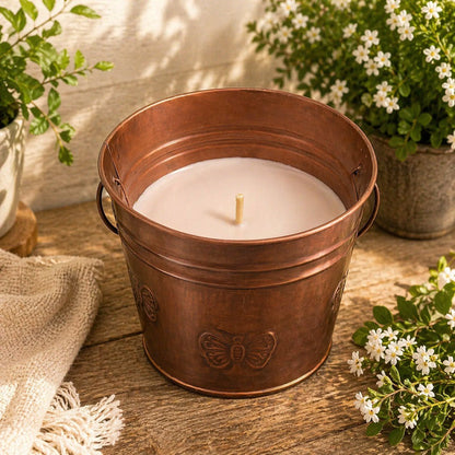 Candle in a copper bucket on a wooden surface with plants around