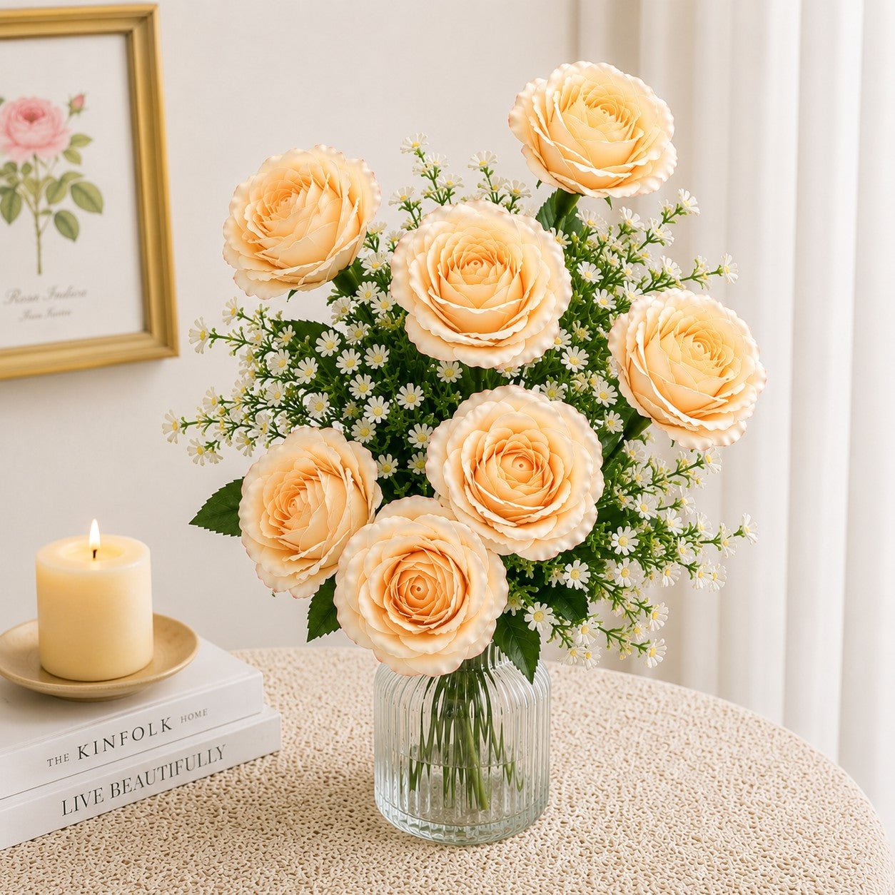 Bouquet of yellow roses in a clear vase on a table with a candle and books in the background.