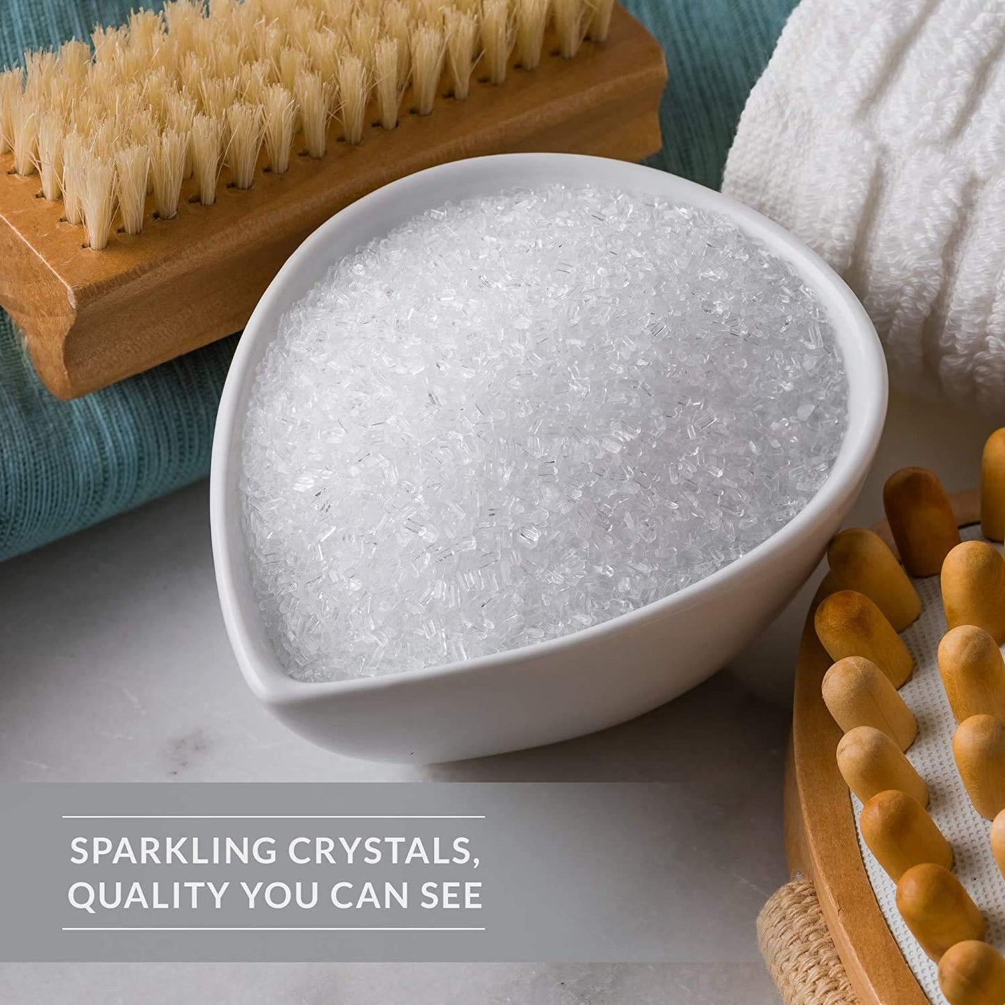 White bowl filled with sparkling crystals on a gray surface with a wooden brush and towel in the background.