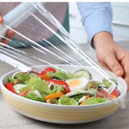 Person covering a salad with plastic wrap on a wooden table
