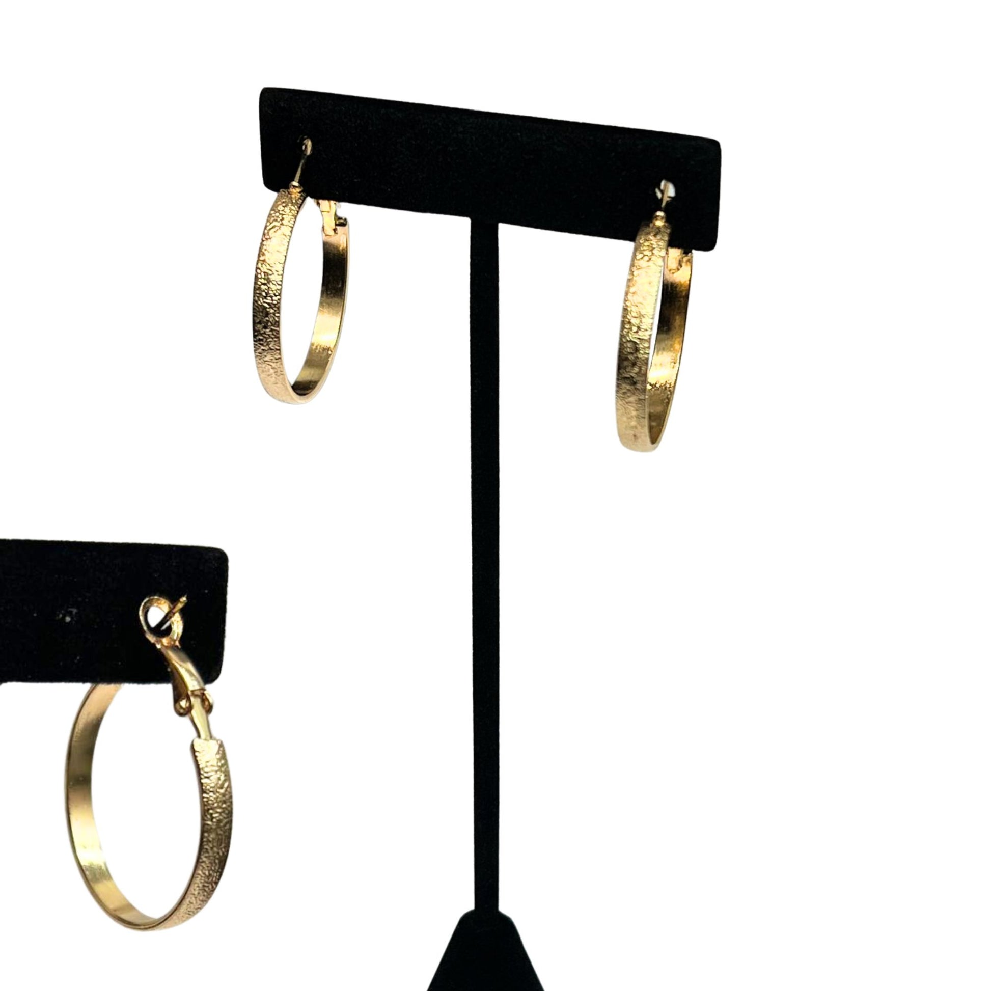Gold hoop earrings on a black earring stand against a white background
