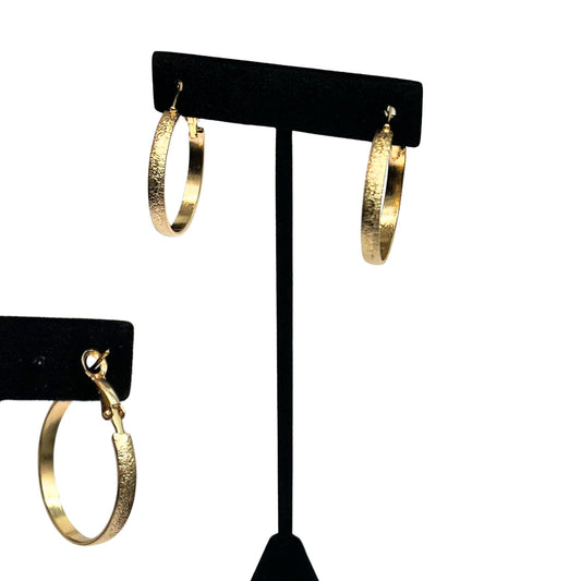 Gold hoop earrings on a black earring stand against a white background