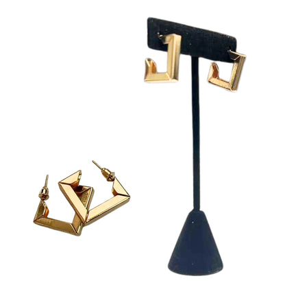 Gold geometric hoop earrings on a black stand against a white background