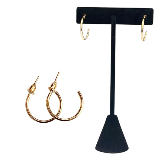 Gold hoop earrings on a black earring stand against a white background