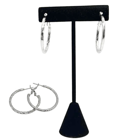 Silver hoop earrings on a black earring stand against a white background