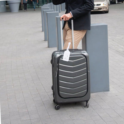 Person pulling a gray suitcase with a tag on a paved street.