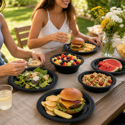 Two women enjoying a meal outdoors with burgers, salads, and fruit on a wooden table.