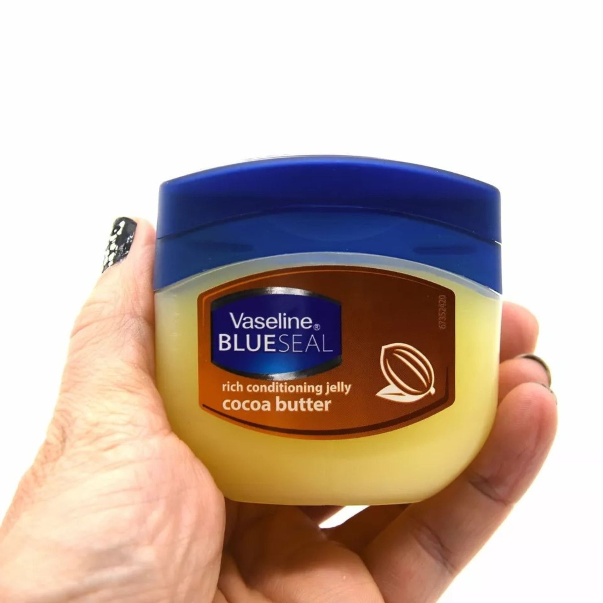 Hand holding a jar of Vaseline Blue Seal rich conditioning jelly cocoa butter on a white background